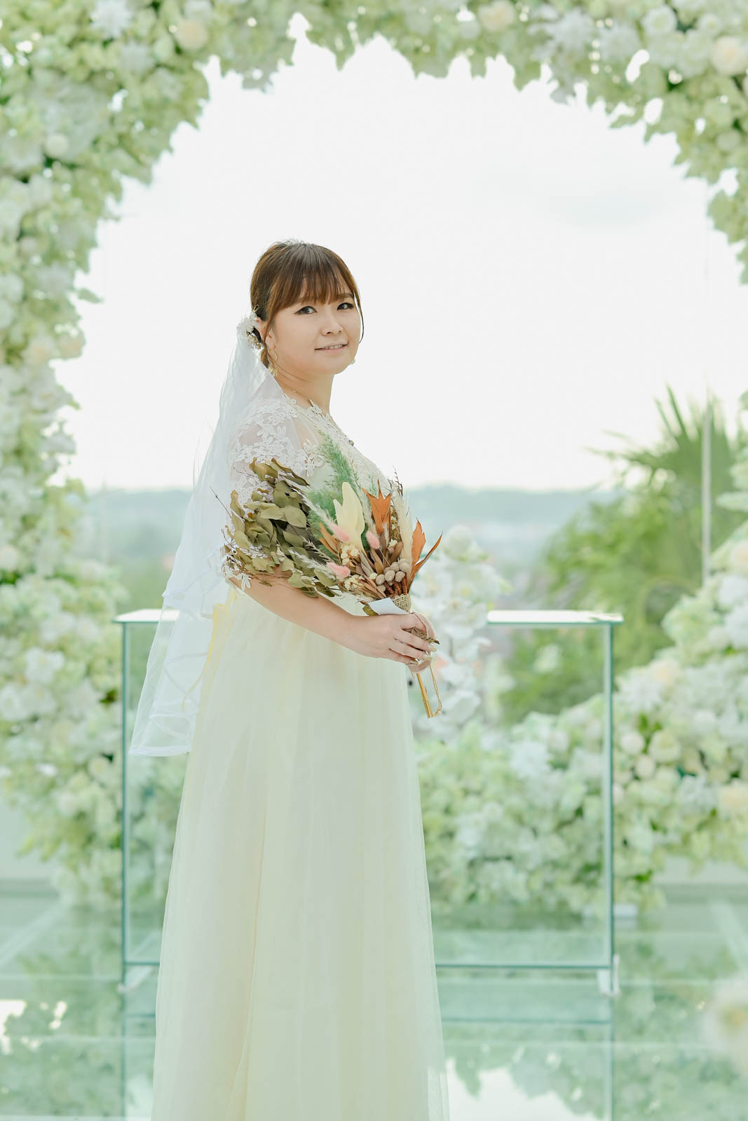 バリ島チャペルの白いフラワーアーチ前でブーケを持つ新婦の前撮りショット