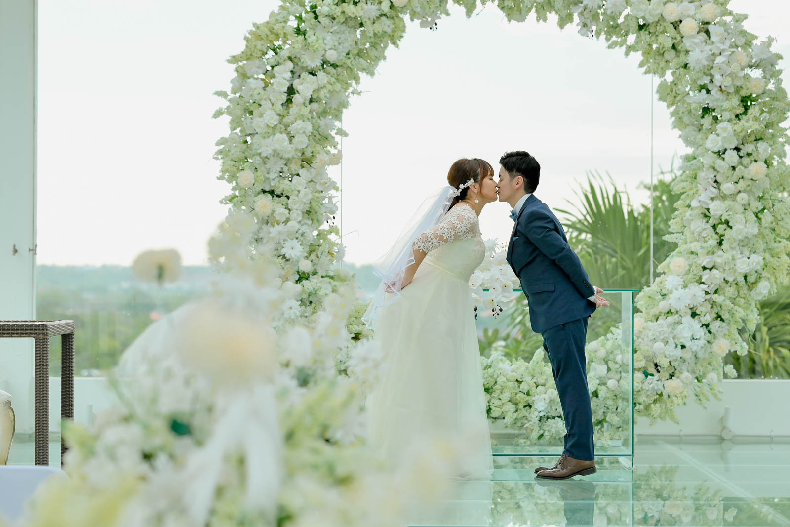 白いフラワーアーチの前でキスをするバリ島チャペルウェディングの一枚