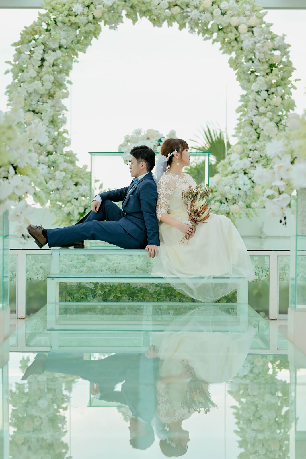 バリ島チャペルのガラス床に反射する新郎新婦の背中合わせポーズ写真