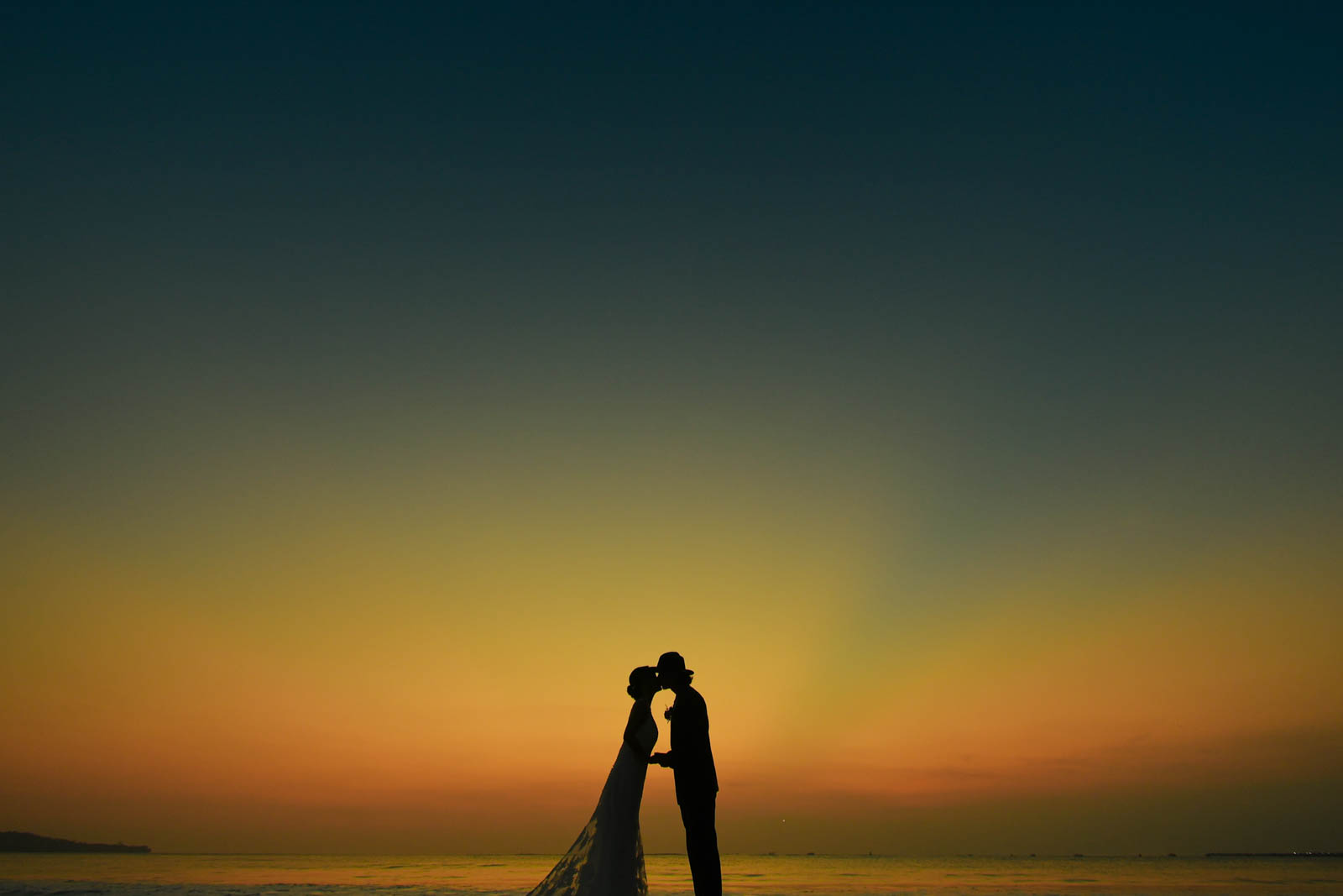 マジックアワーの空の下でキスを交わす新郎新婦のシルエットフォト