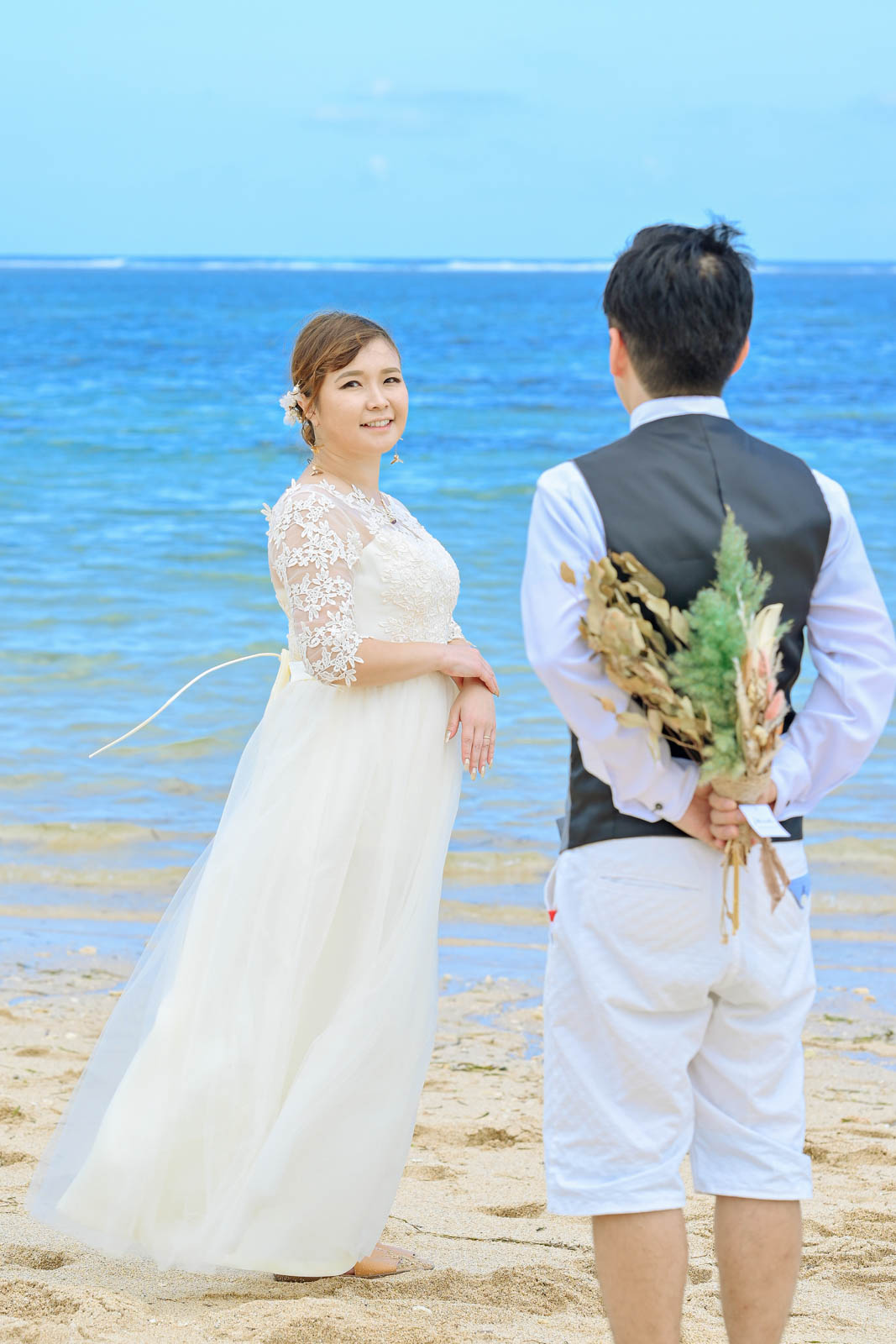 バリ島の海辺で新郎がブーケを背中に隠し新婦を見つめる前撮り写真