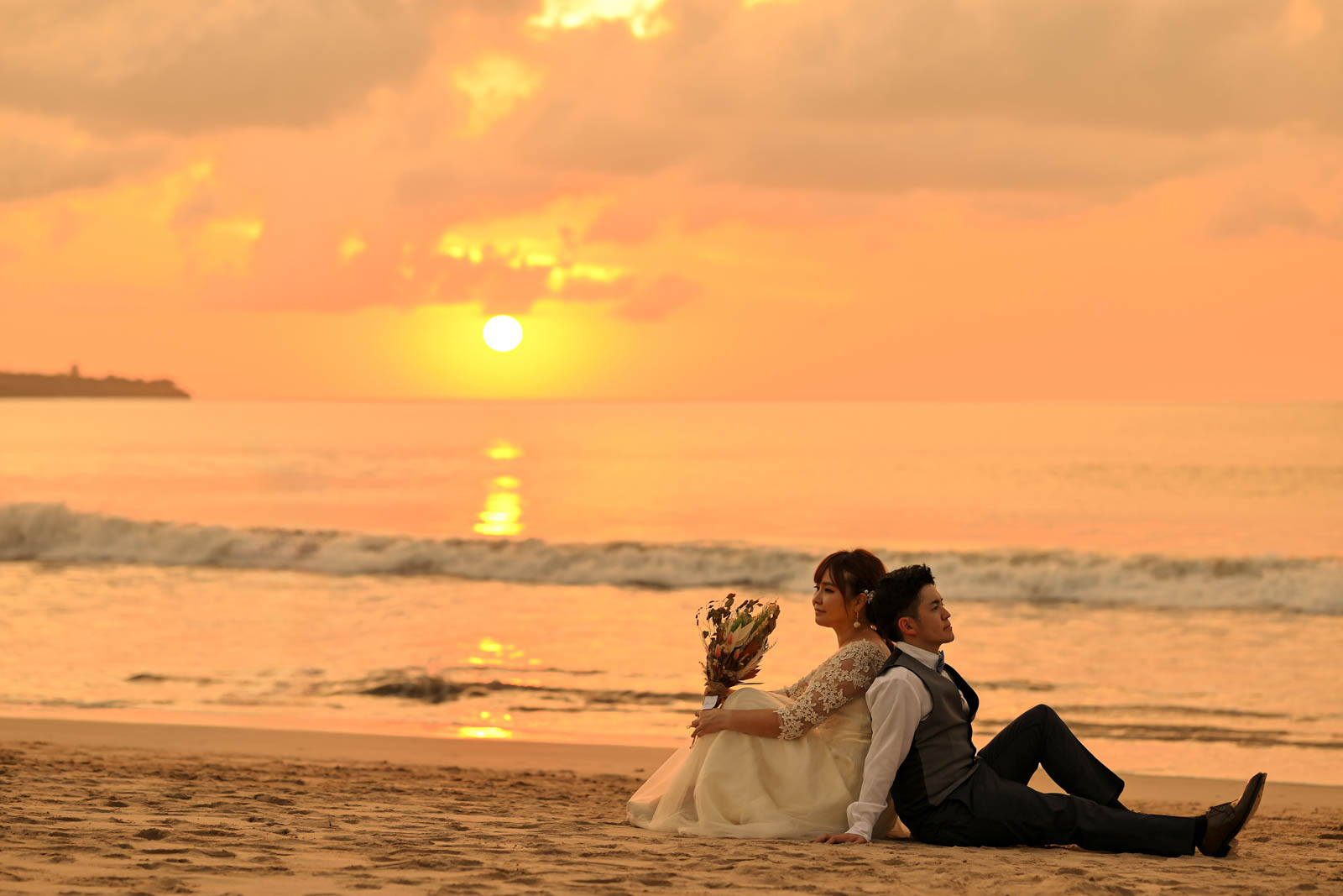 沈む夕日を背景に寄り添って座る新郎新婦のロマンチックなサンセットフォト